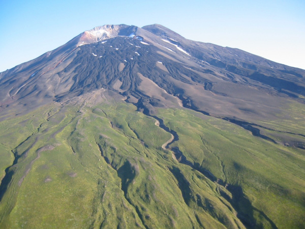 South flank of Gareloi Volcano, showing south summit crater, breached to south, and 1980s-era basalt flows. Much of the flank is covered by 1929 pyroclastics, into which gullies have eroded. Hydrothermally altered area along summit crater rim is the site of persistent fumarolic activity.