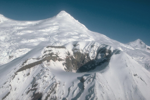 Crater Peak, a satellite vent of Mount Spurr volcano, and the snow- and ice-covered summit lava dome complex of Mount Spurr beyond. View is to the north. Photograph by R. McGimsey, U.S. Geological Survey, 10/9/91.