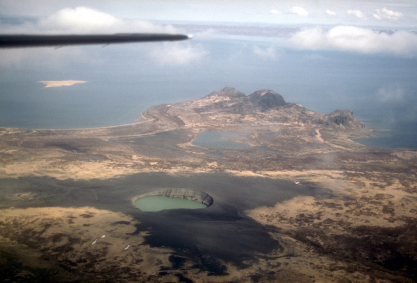 Aerial view, looking north, over the Ukinrek Maars on the south shore of Becharof Lake
on the Alaska Peninsula. The maar craters formed during a 10-day eruption in March and
April of 1977. In the distance (center) are the Gas Rocks, an older volcanic center. Photograph by C. Nye, Alaska Division of Geological and Geophysical Surveys, May 9, 1994.
