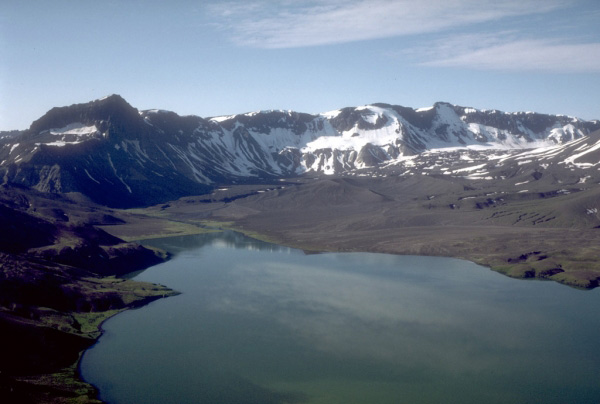 View, looking south, across Aniakchak caldera from its north rim. Surprise Lake and its
outlet are visible at upper left. The prominent dark peak on the left skyline is Black Nose, a high standing remnant of precaldera volcaniclastic rocks. Hummocky ground in the distance against the caldera wall is a pumice-covered glacier and associated moraine. Photograph by T. Miller, U.S. Geological Survey, August, 1985.