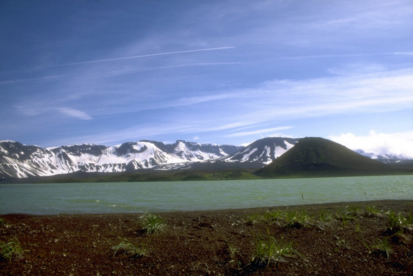 Jet contrails over Aniakchak caldera. The proximity of explosive volcanoes of the Aleutian volcanic arc to North Pacific air routes is one of the principal hazards associated with volcanoes in Alaska. View is to the south. Photograph by C. Neal, U.S. Geological Survey, July 19, 1994.