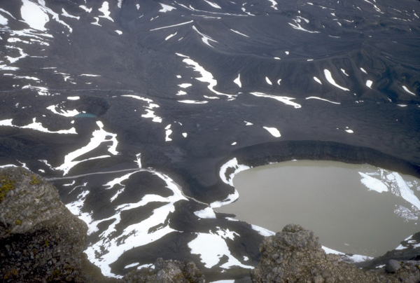 View onto the floor of the caldera from the southeast rim of Aniakchak caldera. Two
explosion craters (maar craters) partially filled with seasonal meltwater are visible. The craters were formed by explosions through older lava flows from Vent Mountain, an intracaldera stratocone. Photograph by R. McGimsey, U.S. Geological Survey, June 29,
1992.