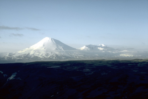 Distant view, looking north, of symmetrical Vsevidof volcano, a historically active, 2,149-m (7,050 ft)-high stratovolcano on central Umnak Island in the eastern Aleutian Islands.  Mount Recheshnoi is on skyline at right. U.S. Geological Survey photograph, July, 1975.