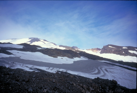 A layer of ash is exposed in melting snow on the upper slopes of Makushin volcano.  The ash is composed primarily of hydrothermally altered rock which gives it a distinctive grey color.  View is from the southwest.