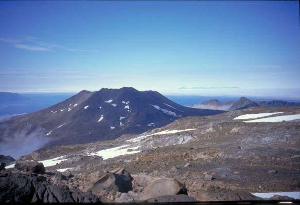 Pakushin, a flank vent of Makushin Volcano, is a cinder cone that was constructed during the Pleistocene.  Okmok caldera is visible in the distance.  View is from the east.