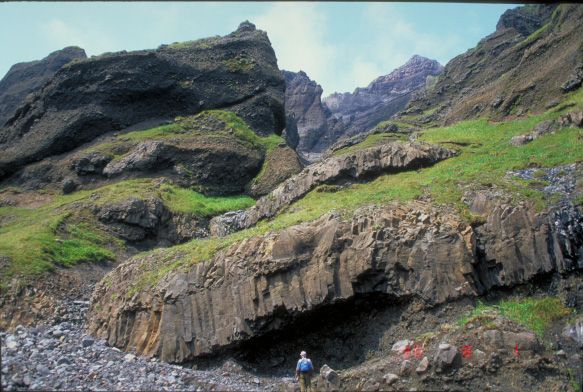 Don Richter examines a lava flow and a massive section of volcaniclastic rocks near Cape Morgan, Akutan Island.