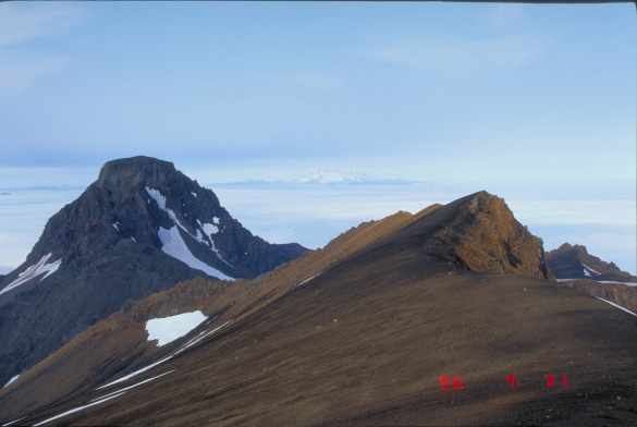 Flat Top Peak, Akutan Volcano.  In the foreground is the rim of older Akutan caldera, located about 1 km south of the modern caldera rim.  Snow-capped Makushin Volcano is visible in the distance.