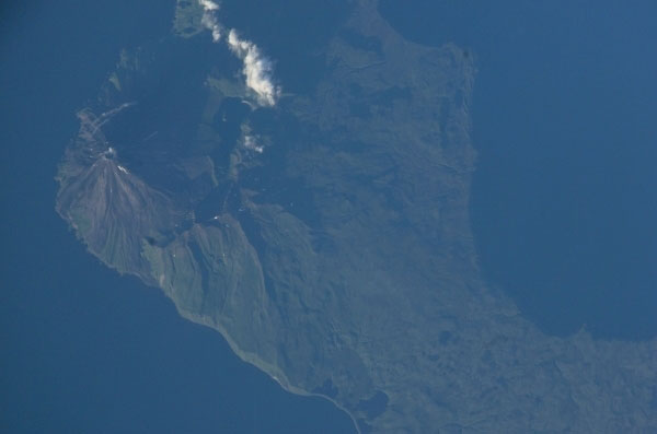 The symmetrical cone of Kanaga volcano stands out on the northern corner of Kanaga Island, located in the central part of Alaska's Aleutian archipelago. Kanaga last erupted in 1994 and is well known for its active fumaroles and hot springs (located, in this image, by fine steam plumes on the northeast flank of the volcano). A small lake to the southeast of the cone is situated on the floor of a larger more ancient volcanic caldera. The crew of the international space station acquired this image late in the day of August 13, 2002. Note how the late summer sun accentuates the terrain features like the volcanic flows that radiate down from the volcano's peak, and the steep cliffs along the western coastline. 

Mission: ISS005 Roll: E Frame: 10097 Mission ID on the Film or image: ISS005
Country or Geographic Name: USA-ALASKA
Features: KANAGA ISLAND, VOLCANO
Center Point Latitude: 52.0 Center Point Longitude: -177.0