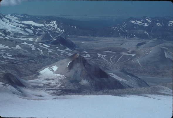 View of the upper Valley of Ten Thousand Smokes, looking west. The prominent feature in the foreground is Whiskey Ridge, composed of Jurassic-aged sedimentary rocks of the Naknek Formation. Two domes in the middle-right are Falling Mountain and Cerberus. Baked and Broken Mountains are visible on the right. In the basin in the center, the vent for the great eruption of 1912 is located, though Novarupta dome is not visible. 