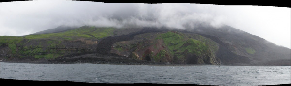Panoramic photo of the western flank of Mt. Cleveland. The very dark deposit that forks down the western side of the volcano is the largest of any of the 2001 lava flows extruded during the February to March eruptions that year. The view is to the east. The northern portion of the lava flow is observed to fork when it encounters the highest part of the newly formed volcaniclastic debris flow fan deposit that was created by the 2001 eruption. Erosion of the fan deposit is very evident in the panoramic creating a higher edge.
