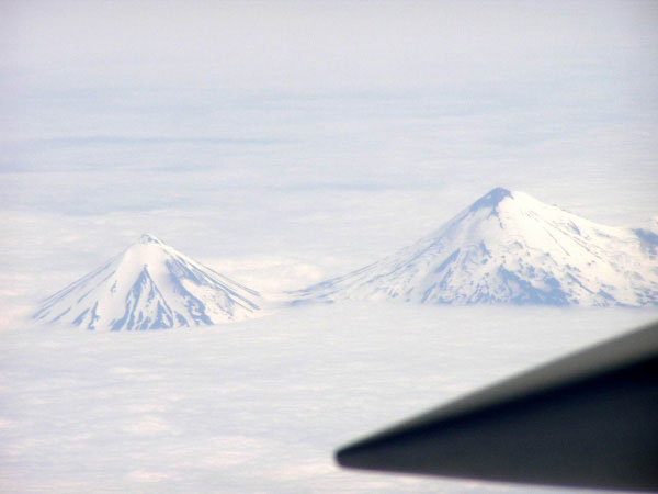 A view from a plane of Pavlof Sister (left) and the larger Pavlof Volcano (right) observed above the clouds over the Alaskan Peninsula. The view is to the south from the plane. The northeastern portion of the summit of Pavlof Volcano (right) possibly displays some minor ash deposits from minor Strombolian bursts, but it could also be a snow-free portion of the summit.
