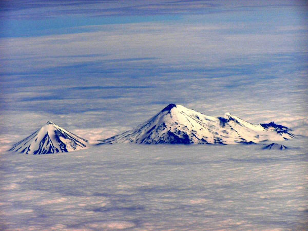 A view from a plane of Pavlof Sister (left) and the larger Pavlof Volcano (right) observed above the clouds over the Alaskan Peninsula. The view is to the south from the plane. The northeastern portion of the summit of Pavlof Volcano (right) possibly displays some minor ash deposits from minor Strombolian bursts, but it could also be a snow-free portion of the summit.