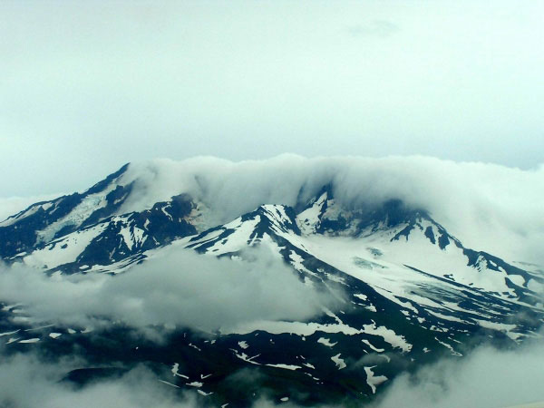Recheschnoi Volcano with clouds draping part of the summit as seen from a plane. The image was re-exposed in order to decrease the glare and haze in the image.