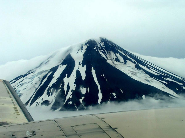 Vsevidof Volcano with clouds draping part of the summit as seen from a plane. The image was re-exposed in order to decrease the glare and haze in the image.