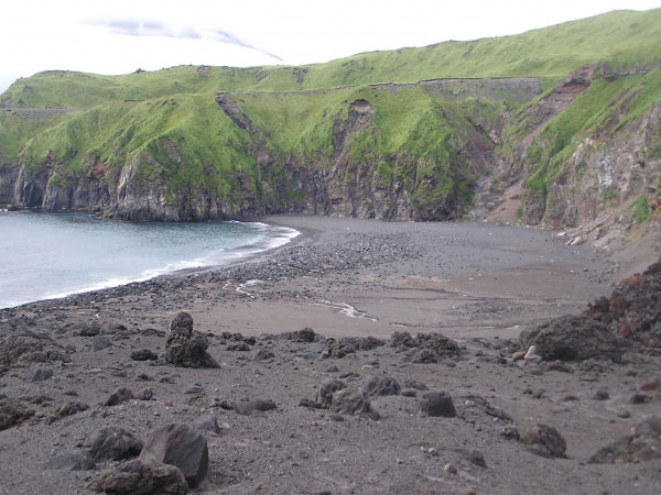 A view of the beach on the northern side of the volcaniclastic debris flow fan deposit that has about tripled in size since the 2001 eruption of Mt. Cleveland. The material in the foreground is from the volcaniclastic debris flow fan. The larger rocks are breadcrust bombs and lava blocks.