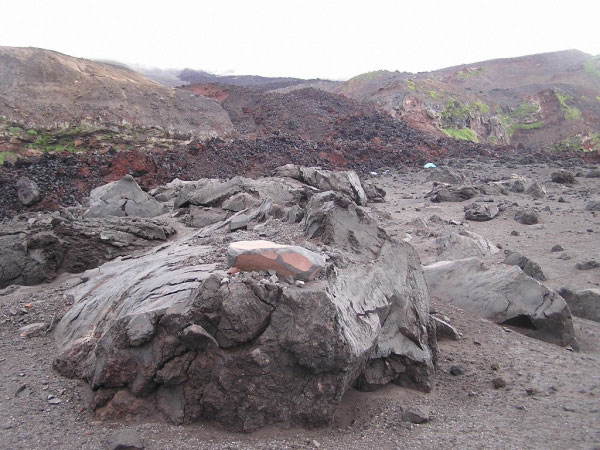 Photo taken from the northwestern part of the newly formed volcaniclastic debris flow fan deposit from the 2001 eruption looking toward the southeast at the large lava blocks and breadcrust bombs (some in combinations of the other as in the one in the foreground). The main 2001 lava flow is observed in the background with the white and teal colored tent (2-man Mountain Hardware Trango for scale) to the right of center indicating the location of the camp. The northwest section of the volcaniclastic fan deposit was where most of the large lava blocks wher located at the surface. The rest of the fan deposit was dominated by breadcrust bombs on the surface.