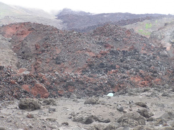 Photo taken from the northwestern part of the newly formed volcaniclastic debris flow fan deposit from the 2001 eruption looking toward the southeast at breadcrust bombs. The northern fork of the main 2001 lava flow is observed in the background with the white and teal colored tent (2-man Mountain Hardware Trango for scale) to the lower right of center indicating the location of the camp. The location of the camp is where this northern fork reached the highest part of the fan deposit, and forked for a second time.