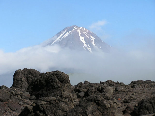 Photo of Mt. Carlisle peaking above the low stratus clouds that would eventually roll in to halt half a days fieldwork on the volcaniclastic debris flow fan deposit created from the 2001 Mt. Cleveland eruption (in foreground). The view is of the southern summit region of Mt. Carlisle.