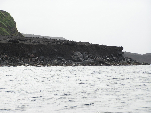Photo of the northwestern half of the volcaniclastic debris flow fan deposit created from the 2001 Mt. Cleveland eruption as observed from the Augusta D. The steepening edge of the fan deposit is evident on the right side of the photo with the large eroded debris just above sea level.