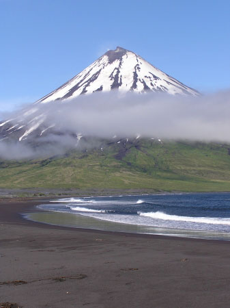 A view from the eastern part of the beach of Applegate Cove of the east-northeastern flank of Mount Cleveland. Fumarolic steam is observed from the southern part of the crater rim (left side of the photo), and from a vigorous fumarole on the eastern side of the summit with some sulfurous deposits also observed (a little downslope from the crater). This view shows the collapsed region of the southern portion of the crater rim (left side of the summit). There was no cut out portion observed by the field party in September 2002. The cut out (collapsed) part was first observed from a similar vantage point - though further out to sea - but due to more cloud cover that day, it was difficult to be certain of the change. This view in 2004 confirmed that some morphologic change took place at the summit since 2002.