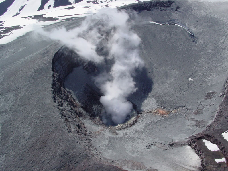Aerial view down into summit crater of Korovin volcano on Atka Island. Roiling pool occupies bottom of crater; ash covers snow and ice  inside crater.  