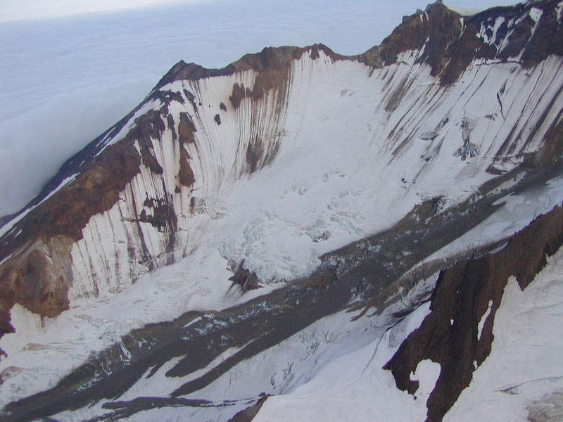 Flow lobes of a dark gray, clay-rich lahar can be seen down the length of the south glacier at Chiginagak Volcano.  The lahar deposits resulted from the draining of the summit caldera lake sometime in early summer 2005. 