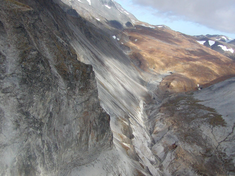 The south glacier at Chiginagak Volcano is covered in orange, hydrothermally altered volcanic rock debris.  Flow lobes of a dark gray, clay-rich lahar can be seen down the length of the south glacier at Chiginagak Volcano.  The lahar deposits resulted from the draining of the summit crater lake sometime in early summer 2005. This photo was taken looking to the east, above the falls.