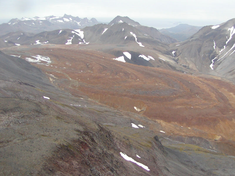 Orange, debris-covered lower lobe of the south flank glacier at Chiginagak volcano.  Flow lobes of a dark gray, clay-rich lahar can be seen down the length of the glacier. The lahar deposits resulted from the draining of the summit crater lake sometime in early summer 2005. 