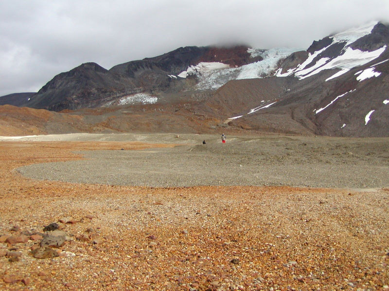 Flow lobes of a dark gray, clay-rich lahar can be seen down the length of the south glacier at Chiginagak Volcano.  Here near the base of the glacier, the gray deposits stand in stark contrast to the orange-brown older surface of the glacier.  The lahar deposits resulted from the draining of the summit caldera lake sometime in early summer 2005. 