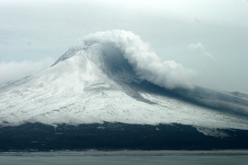 Augustine Volcano. Image taken during 1/16/06 gas overflight after the explosive events of 1/13/06 and 1/14/06. Image taken from the southwest looking at the steam plume hugging the slopes as it travels to the south. Debris flow deposits visible on the southern slope.