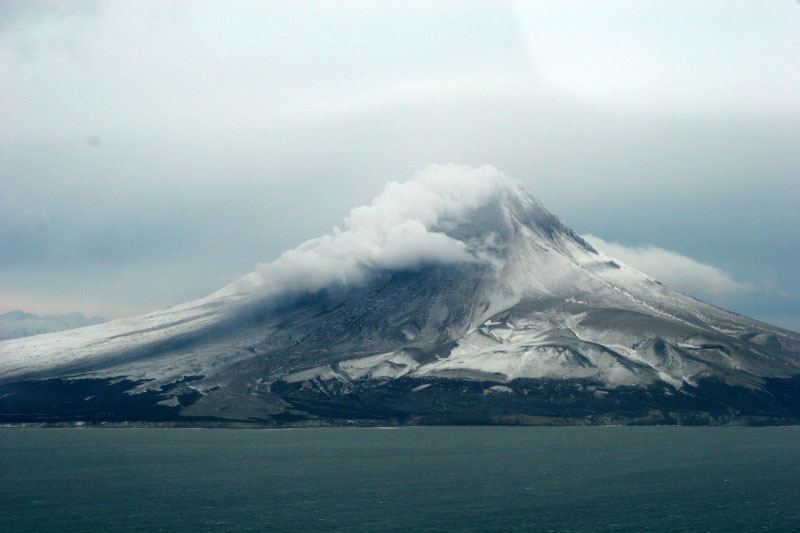 Augustine Volcano. Image taken during 1/16/06 gas overflight after the explosive events of 1/13/06 and 1/14/06. Image taken from the southeast showing the steam plume as it travels to the south and pyroclastic flow deposits that extend to the southeast coast (some of which make ocean entry). Most of the pyroclastic flow deposits were constrained to the southeast sector but a few were observed on the north side of the volcano. 