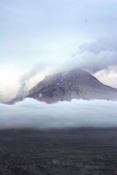 Augustine Volcano on 1/29/06 observation overflight.  Photo of west and north flanks of the volcano. White steam and gas on mid and lower north flank is from a recent pyroclastic flow deposit on the north flank (probably emplaced within an hour of the photo being shot).  The main ash and gas plume is drifting to the S SW.