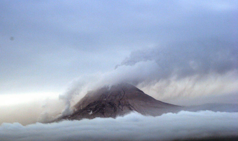 Augustine Volcano on 1/29/06 observation overflight.  Photo from the west with view of north and west flanks of the volcano. White steam and gas on the north flank is from a recent pyroclastic flow deposit on the north flank (probably emplaced within an hour of the photo being shot).  The main ash and gas plume is drifting to the S SW.  Ash fall from the main plume can be seen below the plume to the south.