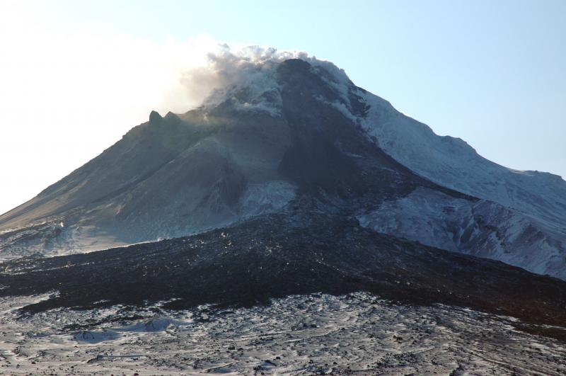 The north flank of Augustine Volcano as seen from the spot radiometer site at Burr Point.  In spite of bad lighting, the photo shows both the summit dome and rubbly northern lava flow just below the dome.  The middle of the photo shows the large fresh fan of debris that continues to fall from the dome and flow.  The east flank (left) of Augustine is covered by thin dusting of new ash.  The entire summit area is steaming.