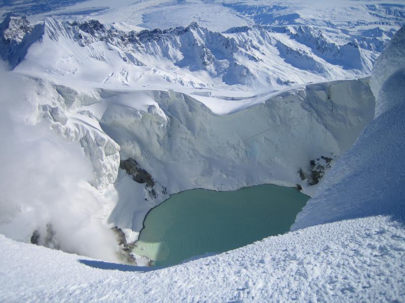 View from the summit ridge of Mt. Spurr down into the ice cauldron.  Part of the turquoise lake, bare warm steaming ground (rock?), and steam rising off of fumaroles are visible.  