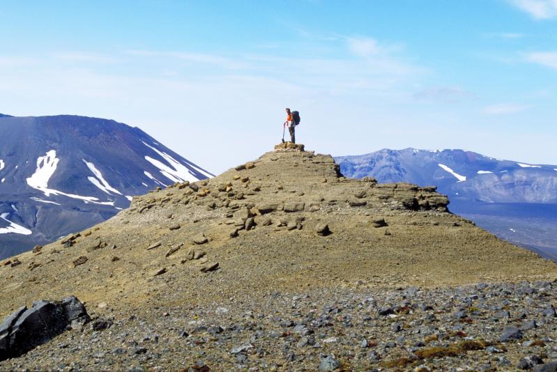Geologist Tina Neal on the summit point along the caldera rim above north wall of The Gates, Aniakchak volcano. Here, volcaniclastic sedimentary rocks are overlying bedrock of the Naknek Formation. 