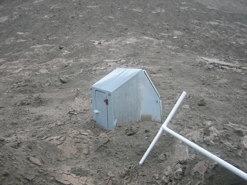 Hut and tipped over solar panels for AVO4, a seismic station on Augustine Island. This station was damaged during the 2005-2006 eruption of Augustine - this photo shows it surrounded by 2006 ash and ballistics.