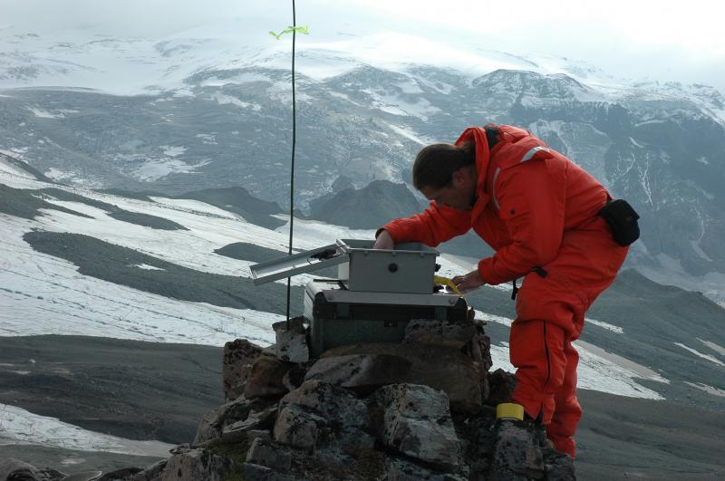 Photograph of AVO staff Rick Wessels installing time-lapse camera west of Fourpeaked volcano.  The camera is looking E SE at the summit area of the volcano.  On a clear day, the summit craters are in full view.