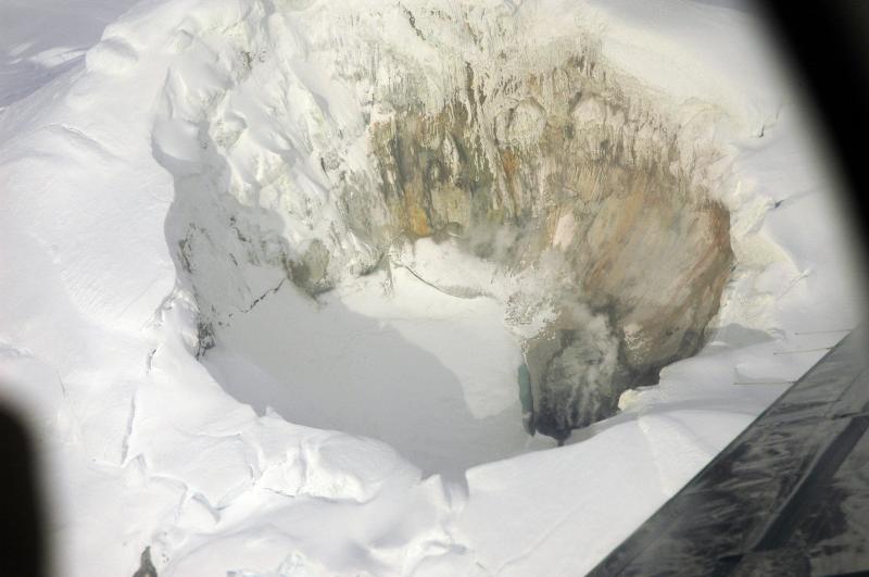 Summit ice cauldron of Mount Spurr.  The lake is now mostly frozen and snow is accumulating, ramping up the southwest wall.  A narrow strip of ice-free water exists along the northeast shore, adjacent to the still-very-active fumaroles.