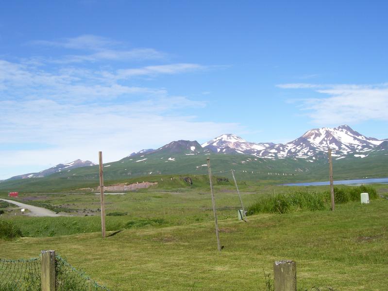The left most peaks belong to Korovin Volcano, with the current activity of Korovin just out of view behind the left most post. The conical peaks roughly in the middle of the horizon are of Kliuchef Volcano.