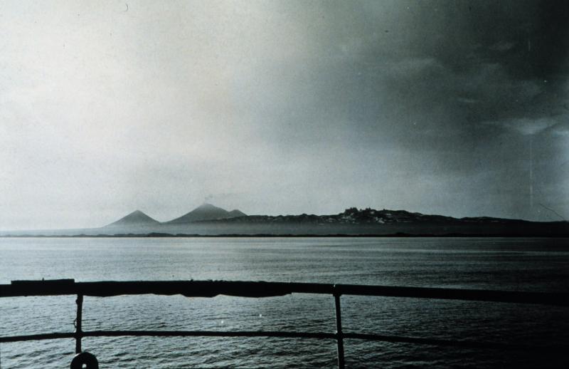View of Pavlof steaming.  Peak behind and to the left (west) of Pavlof is Little Pavlof; peak slightly behind and to the right (east) is Pavlof Sister. Aighileen pinnacles are farther to the right. Photograph from the Coast and Geodetic Survey Season's Report Bowie 1956-29. Photograph from National Oceanic and Atmospheric Administration/Department of Commerce Photo Library, America's Coastlines Collection.