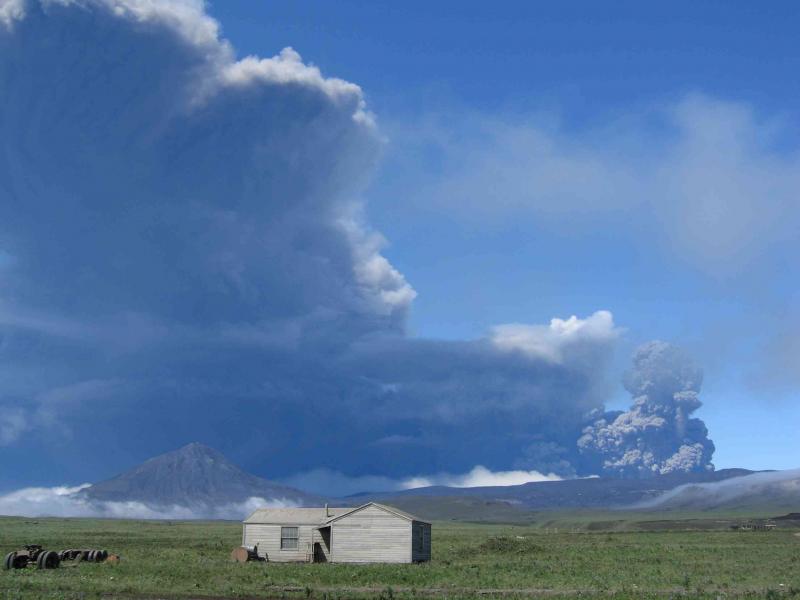 View of the eruption plume as seen from Fort Glenn (ranch building in foreground) on 8-03-2008. The small peak to the left is Tulik, an extra-caldera stratocone.
