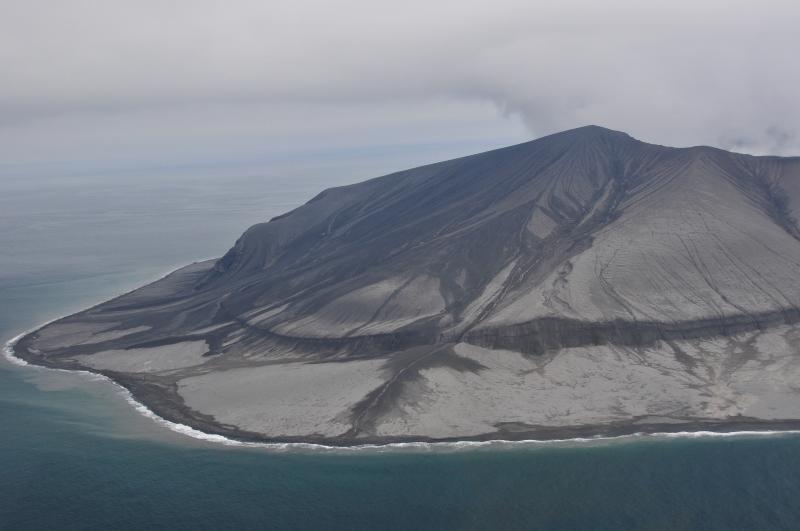 Aerial view of the southwest flank of Kasatochi volcano, August 22, 2008. Fine-grained pyroclastic surge and fall deposits produced during the waning stages of the eruption mantle the surface. These deposits are about 1-2 m thick and overlie much coarser grained pyroclastic-flow deposits emplaced as hot, fast-moving granular flows. The pyroclastic flows deposited gravelly material on the flanks of the volcano and extended the shoreline about 400 m. The prominent cliff like feature that rims the lower third of the volcano is a wave cut cliff along the former shoreline. Tide gage data from nearby Adak Island indicates that a 20 cm amplitude tsunami was associated with the eruption and most likely was initiated when the pyroclastic flows entered the sea.