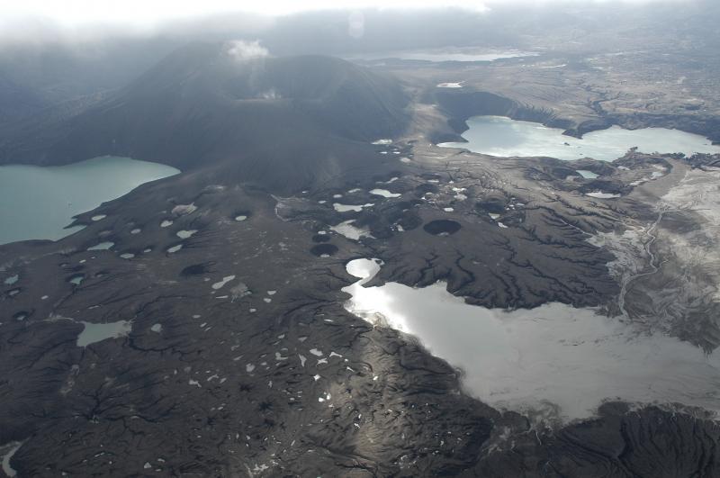 View to the south across the Cone B lava flow terrace, pocked by small irregular ponds where rainwater has collected and the Cone B lake at lower right.  The circular crater field is interpreted to be a zone of explosion craters that blasted through 1997, 1958 lavas early in the eruption.  They were then blanketed by many meters of ash and lapilli, and now they are widening as material collapses into the craters.  The 'old' Cone D lake is at upper left, the 'new' lake at right middle, and the Cone C lake is in the very far ground beyond the new tephra cone, which is on the order of 800-900 feet above the level of the old lake.  