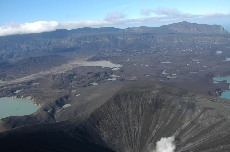 View looking north from above the main new tephra cone (steaming visible at lower edge)across the field of explosion craters towards Cone B and the northern caldera rim.  Prominent white colored walls in the lake cliffs at lower left are formed by dry pyroclastic material, still quite fine grained, as opposed to everything else that is moist to wet to totally saturated.  Where we were able to access this material in the old lake wall, it was only slightly warm.