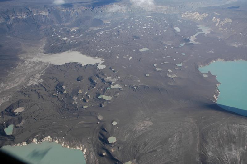 Main 2008 new tephra cone is at lower right.  View is to the north, Cone B at top below Crater Creek basalt cliffs exposed in caldera rim.  What is left of the 'old' Cone D lake is at right, the 'new' lake is at lower left, each partially formed by explosion craters that contribute to the scalloped shape of the lake shorelines.  The many smaller (but still large, maybe 100 - 300 m across) circular craters in the middle ground are likely explosion craters blanketed by later ash fall and surge deposits, and now re-appearing as material falls into the pits.  They have no ejecta blankets that we could recognize - probably because they formed fairly early in the sequence.  The many small irregularly shaped bodies of water on the Cone B flow are ponds trapped by the nearly impermeable muddy layers in the tephra sequence.  It is a muddy, sloppy place to walk about, and the vertical faces on the walls of these craters are very unstable.  