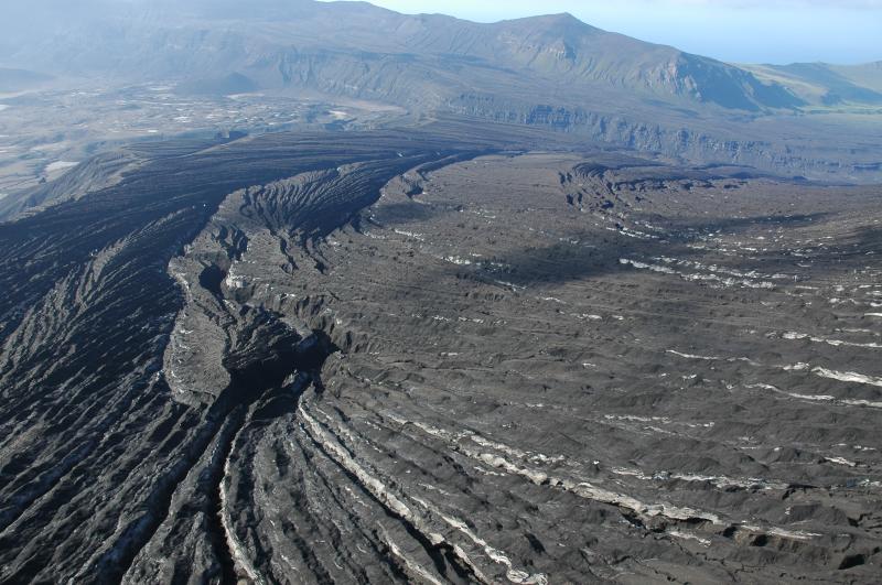 Looking NNW from the east rim of the caldera, the Gates are visible just beyond the rilled terrain.  Estimated tephra thickness here is at least 2 m, but we did not have time to stop and try to dig a section.  Note the pre-eruption snowpack exposed in the rills. Heavy rains have eroded deep gullies rapidly everywhere that abundant ash fell. Station OKER is on a ridge out of the photo to the right, we could not land there easily to check it out.  