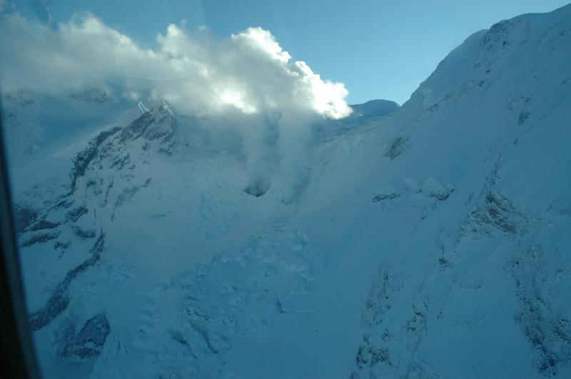 View of vigorous hot fumarolic emission from two holes (at about 7000 feet in elevation) through the steep Drift glacier that descends from the Redoubt summit crater to the north into Drift River Valley. The orifice on the left was first observed on January 30 during an overflight and it appears to have widened by the time this photo was taken on January 31.  The orifice on the right was first seen on January 25. Water vapor and volcanic gas emanating from these holes in the ice are forming a visible white plume that rose about two thousand feet vertically, nearly to the summit of the volcano.