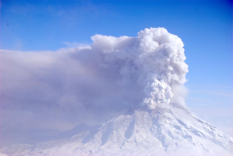 Photograph of Redoubt Volcano in eruption taken during observation and gas data collection flight on March 30, 2009. View is to the east. Continuous emission of volcanic gas, water vapor, and ash is producing a plume rising to about 15,000 feet above sea level. The haze at left below the drifting cloud is a region of active ash fall.  AVO scientists observed ash falling up to 25 miles downwind. 