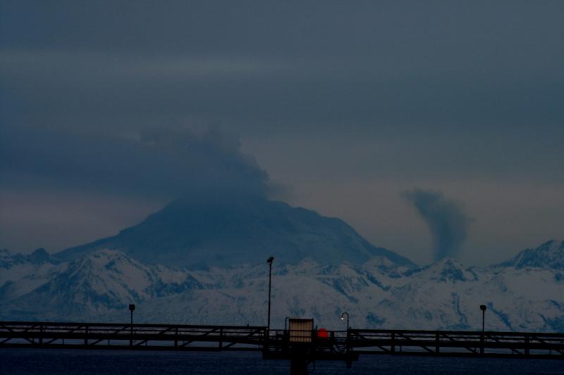 Photo of Redoubt Volcano taken Sunday morning by Rick Monyahan of the Nikiski Fire Department.  At what appears to be the north base of the volcano, a secondary plume is rising to an elevation of about 10,000 feet.  This is likely to be mostly water vapor and very minor amounts of steam rising from an area impacted by hot debris from yesterday's explosion (4/4/09).  The hot material will intermittently interact with  ice, snow, and water to produce small plumes.	